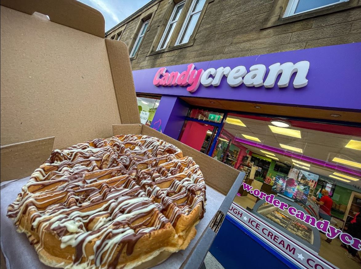 Fresh golden waffle drizzled with chocolate sauce, held in front of the Candy Cream 
dessert shop in Bathgate 