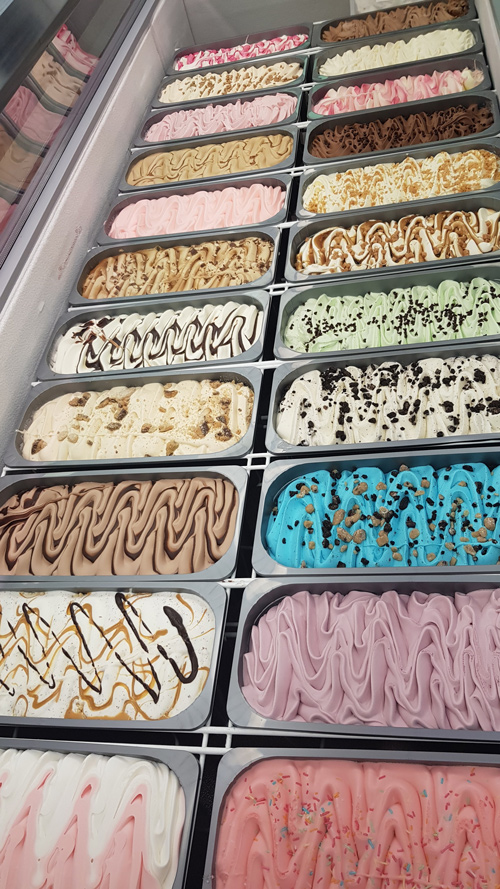 Display case showcasing multiple tubs of colourful artisan ice cream and gelato 
flavours at Candy Cream shop in Bathgate