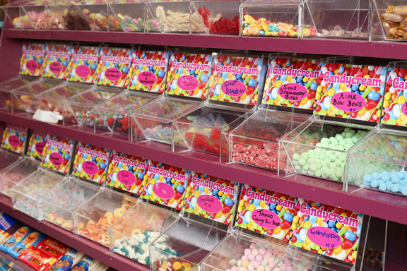 view of the self-serve Pick 'n' Mix wall at Candy Cream Bathgate, showing colourful 
bulk candy, jelly sweets, and bubblegum in clear bins with price labels