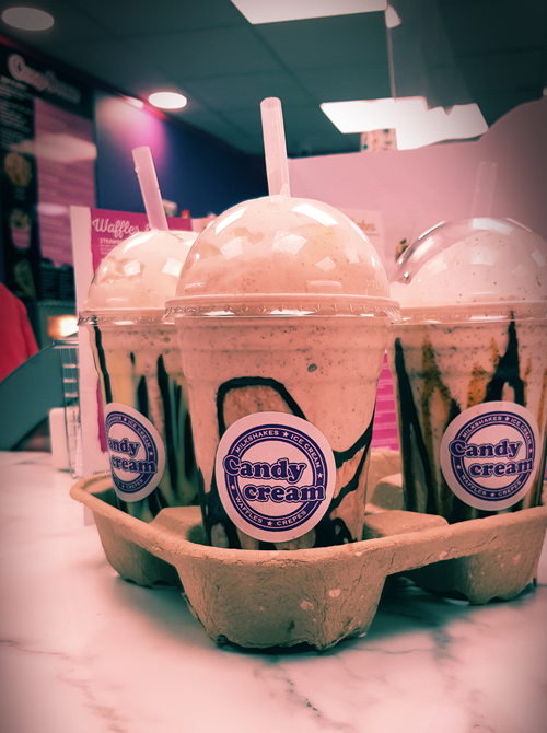 Three fresh milkshakes with chocolate drizzle and Candy Cream logo stickers, ready 
to be served in a carry tray at the Bathgate dessert shop