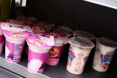 Shelf display of brightly packaged pink tubs of JimJam Candy Floss, a grab-and-go 
sweet product available at Candy Cream Bathgate